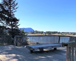 A wooden deck with a bench, overlooking a body of water and a distant mountain.