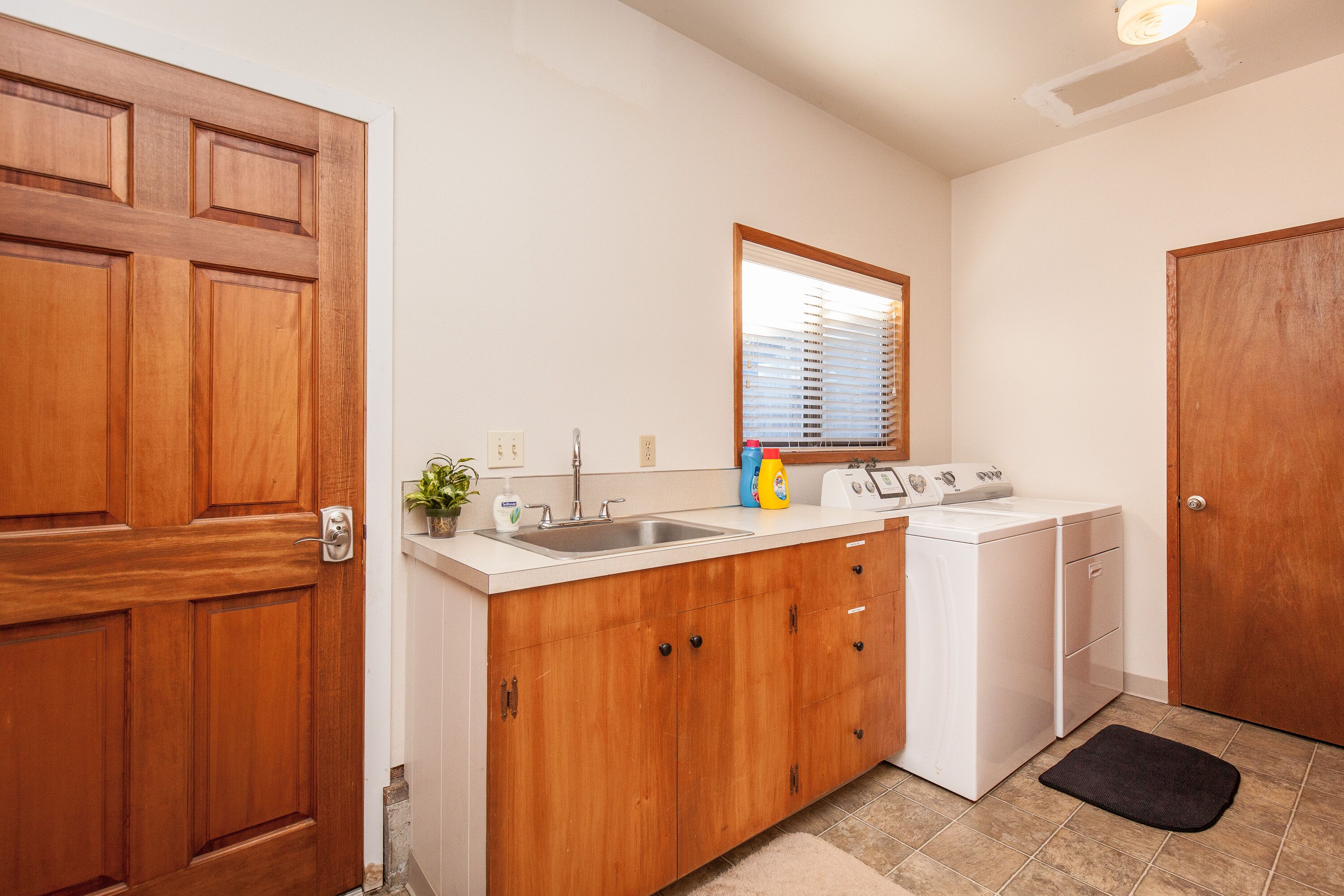 A kitchen with wooden cabinets, a sink, a washing machine, and a window with blinds.