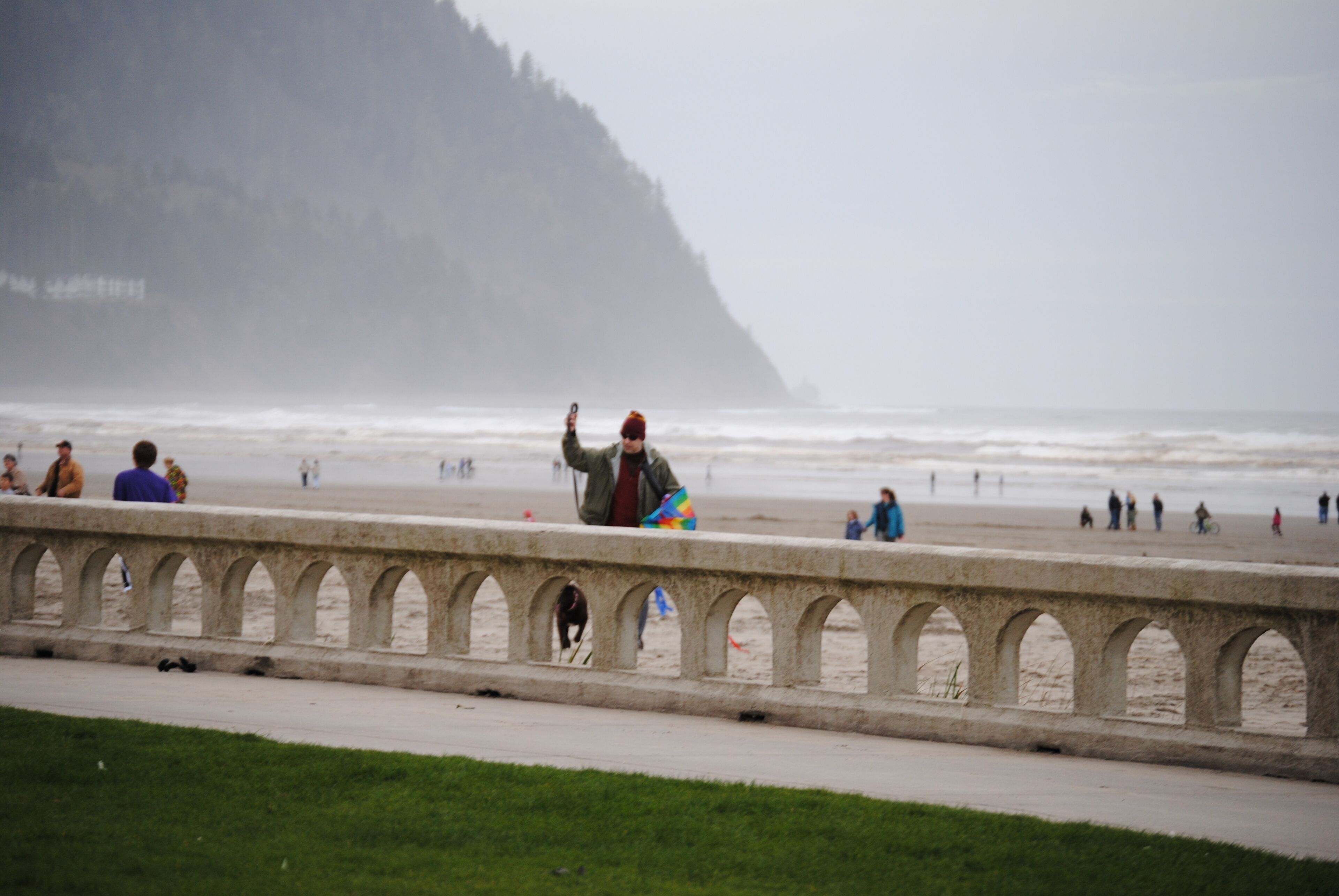 Une promenade en bord de mer agrémentée d’une balustrade en pierre, où l’on peut voir des personnes se promener sur la plage, le tout baigné d’une brume épaisse.