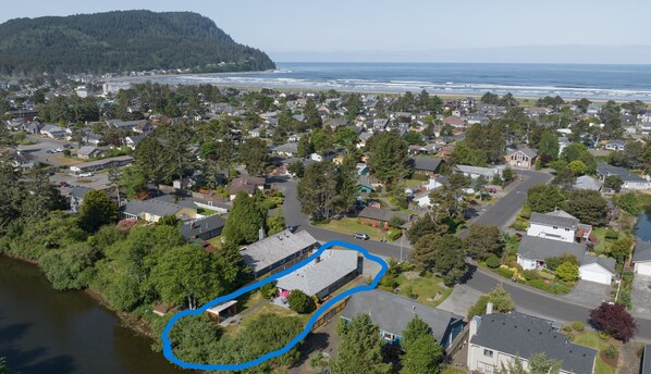 An aerial view of a residential area with houses, a river, and a beach in the background.