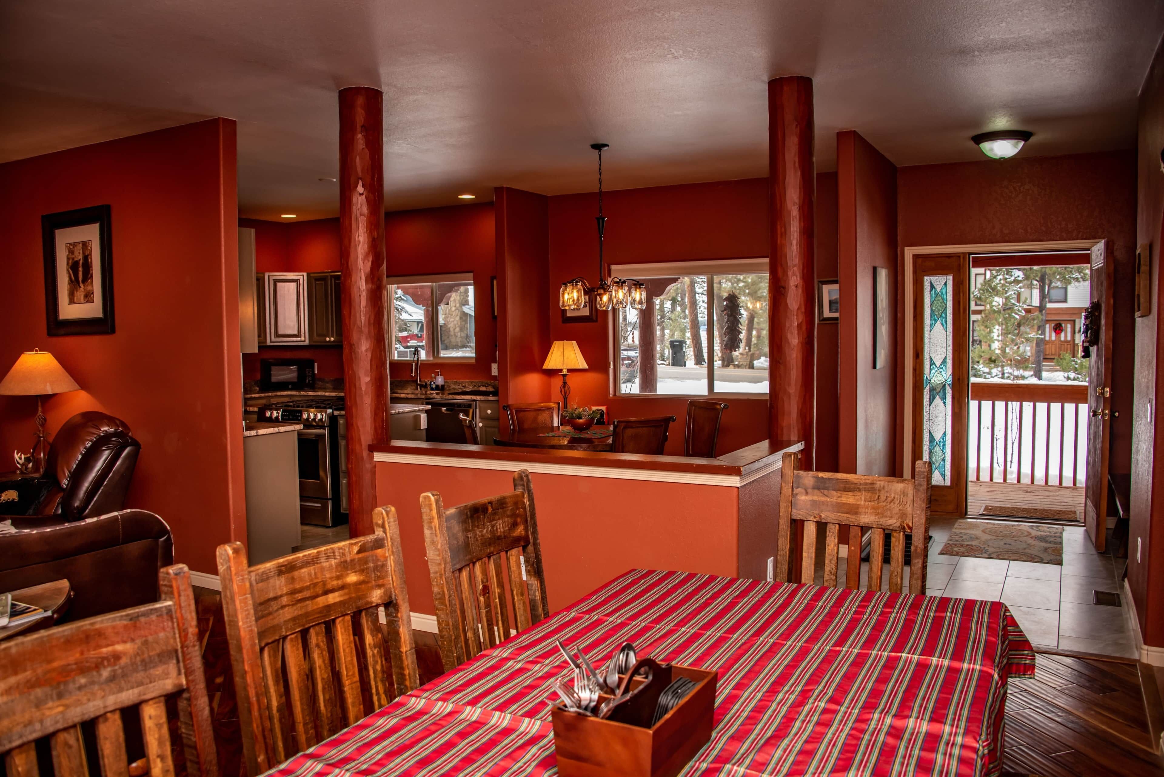 A dining area with a red-striped tablecloth, wooden chairs, and a central island with a lamp.