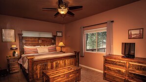 Un dormitorio con una cama de madera, una mesita de noche, un aparador, un ventilador de techo y una ventana con vistas a árboles.