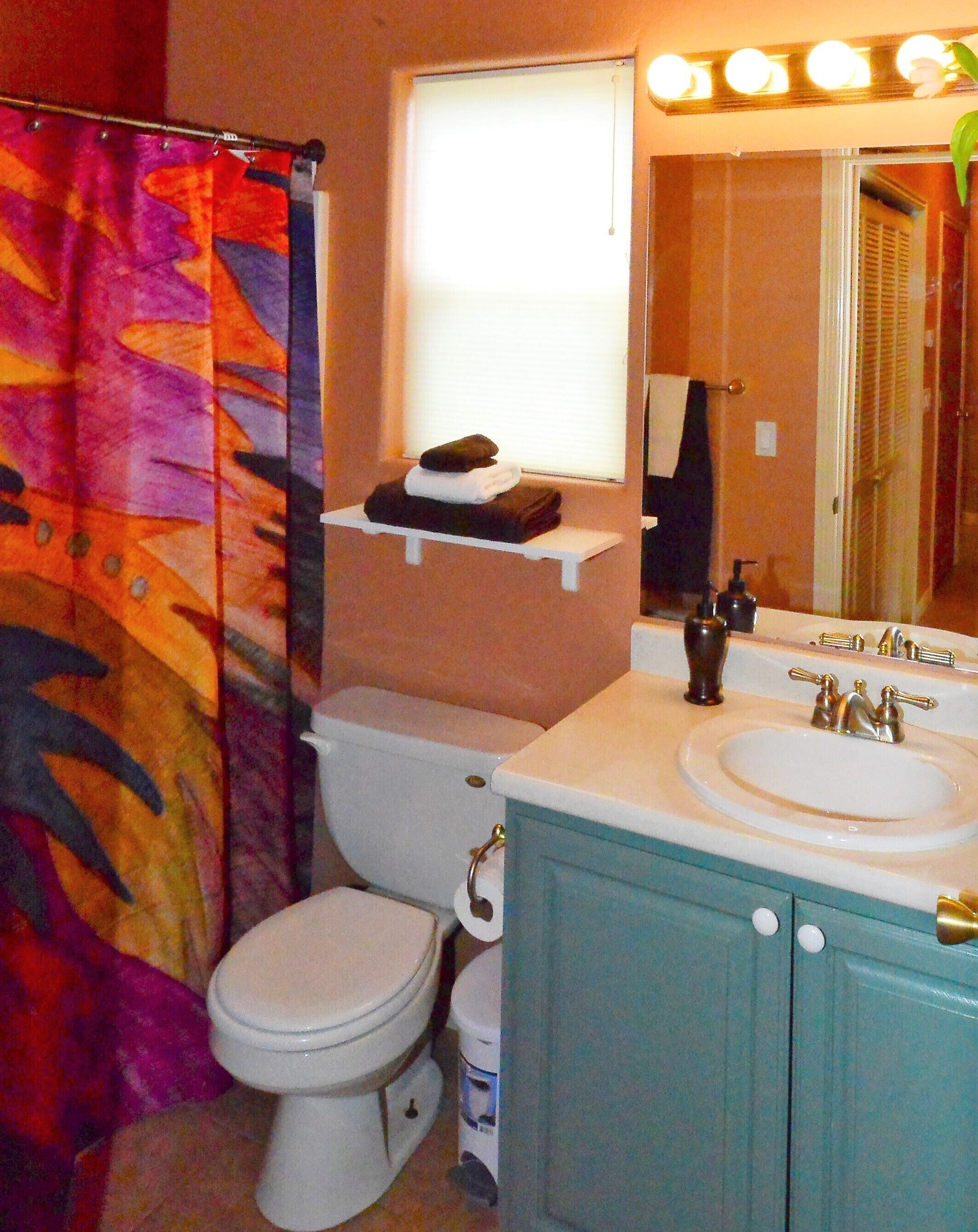 A bathroom with a white toilet, a sink with a mirror above it, and a colorful shower curtain.