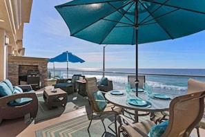 Relax on the patio with unobstructed ocean views, surrounded by comfortable seating and shade from large umbrellas.