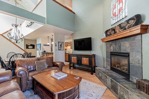 A spacious living room with a leather sofa, wooden coffee table, and a stone fireplace.