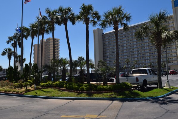 Un hotel con diversi piani, palme e un'area di parcheggio con un pick-up bianco.