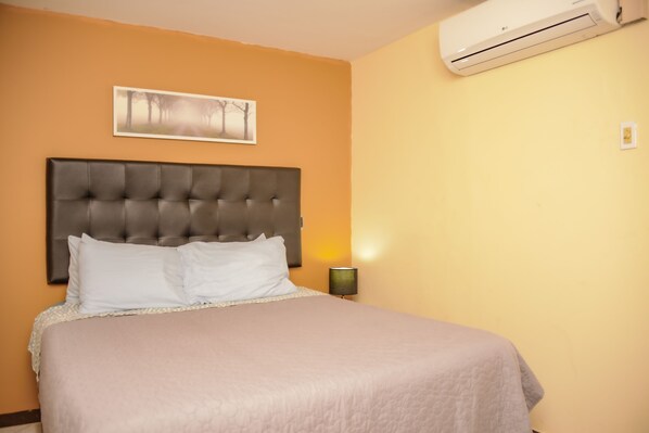 Una camera da letto con un letto grande, una testiera, un condizionatore d'aria a parete e un quadro incorniciato sopra il letto.