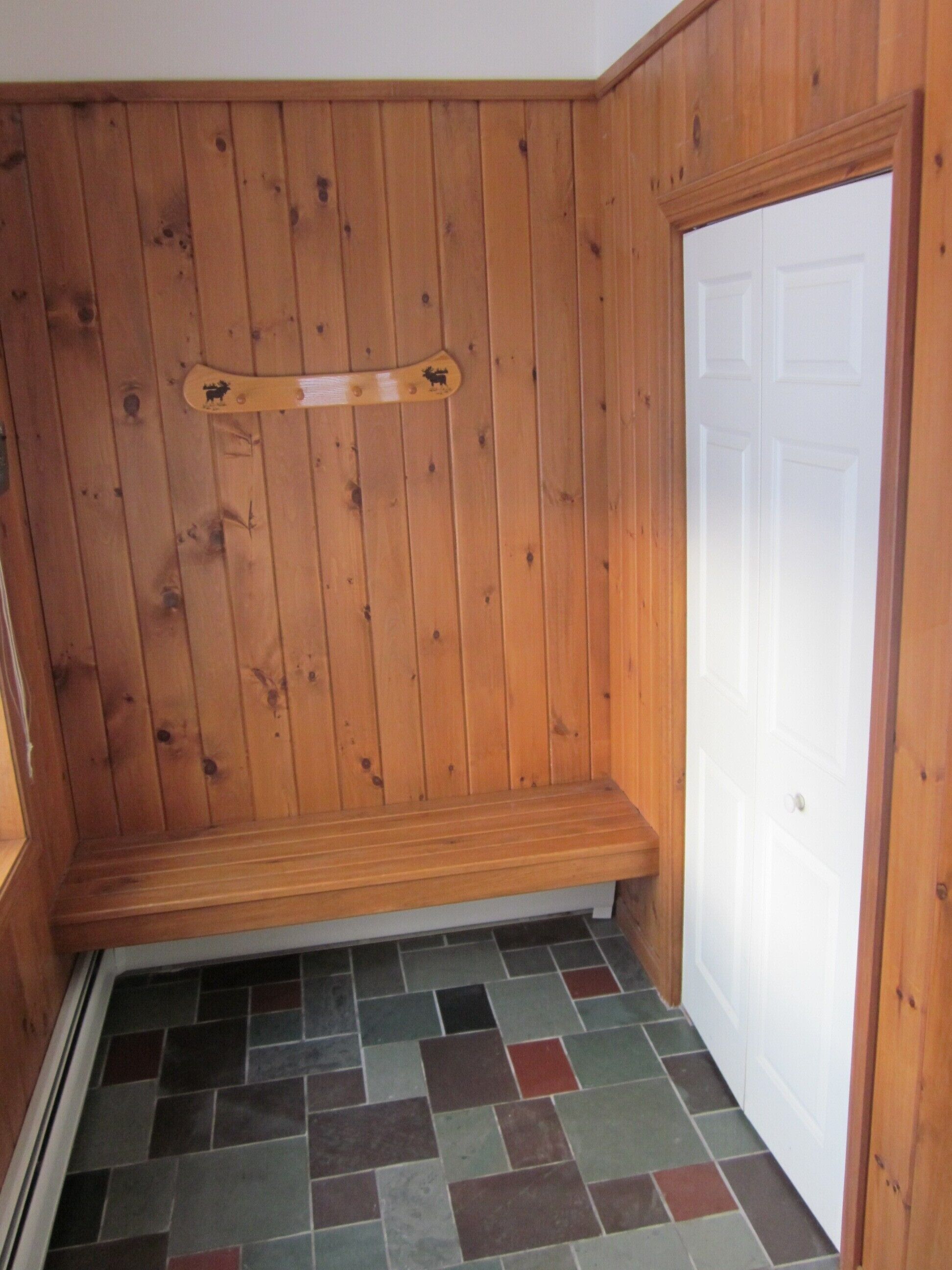 A wooden-paneled room with a bench, a tiled floor, and a white door.