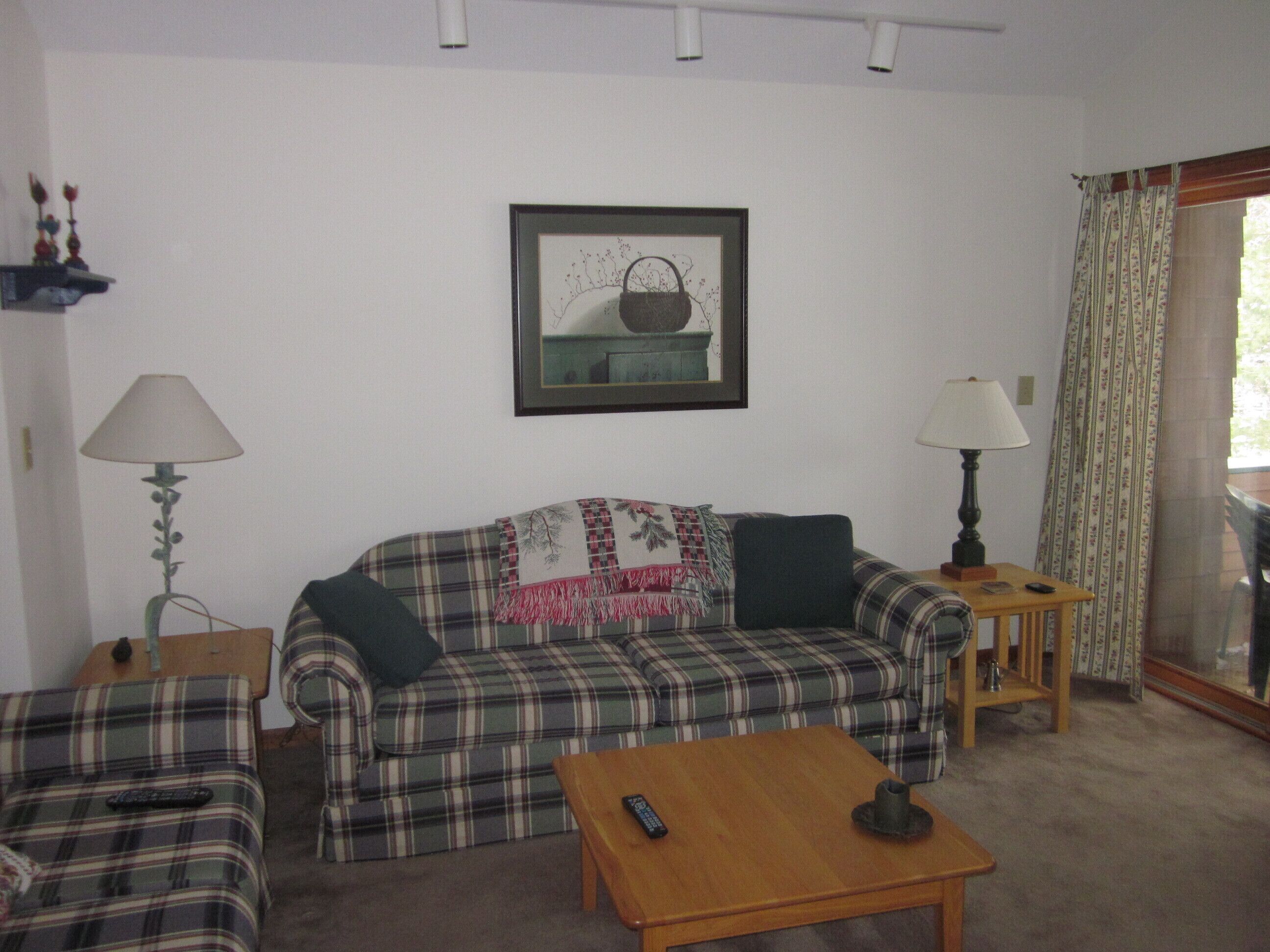 A living room with a plaid sofa, two armchairs, a coffee table, and a framed picture on the wall.
