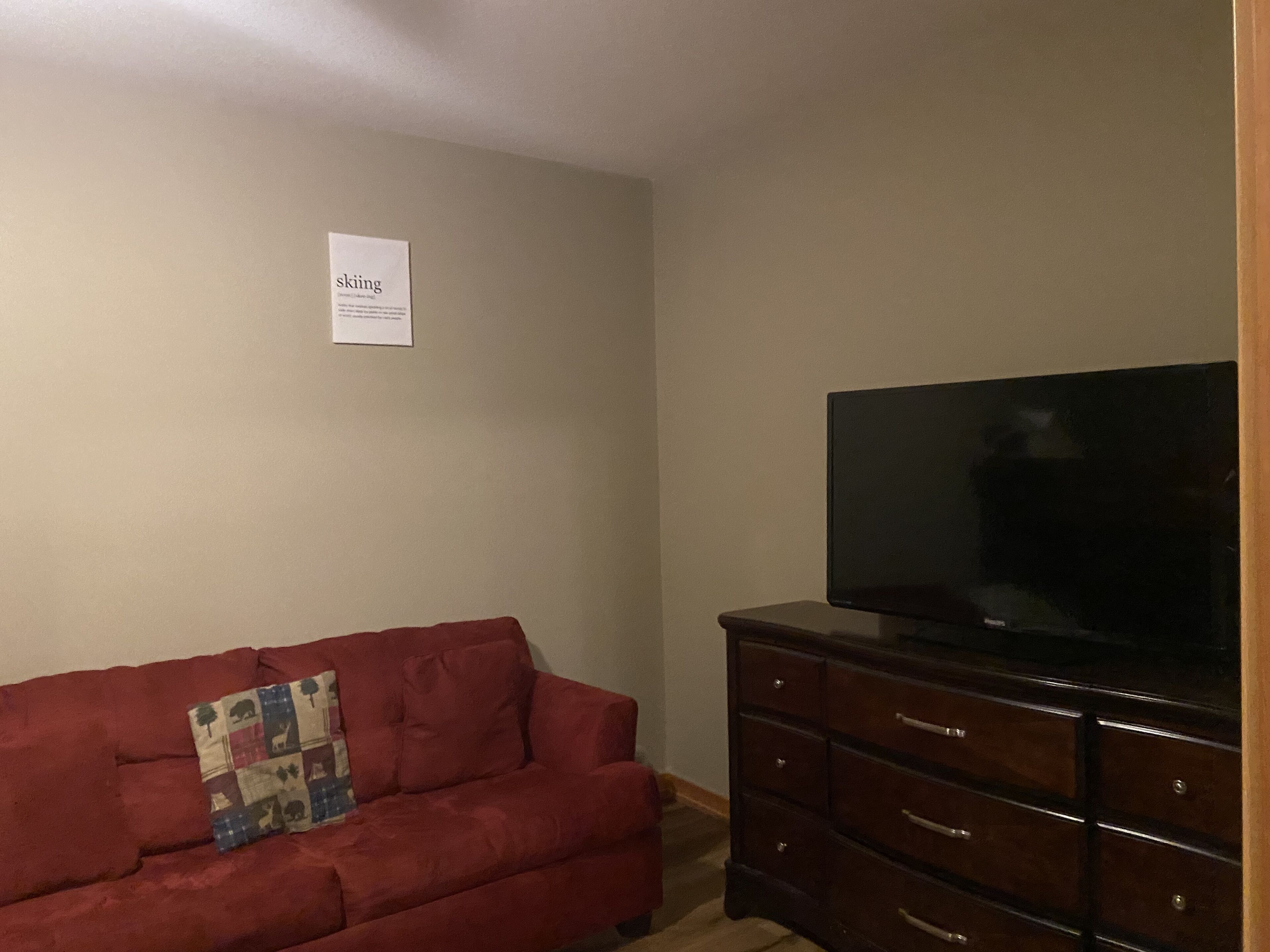 Een woonkamer met een rode bank, een flatscreen televisie op een houten kast en een bord aan de muur.