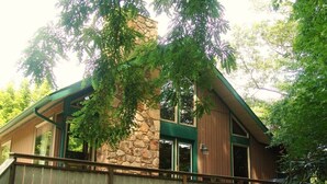 Une maison à deux étages avec une façade en pierre, de grandes fenêtres et une terrasse en bois.