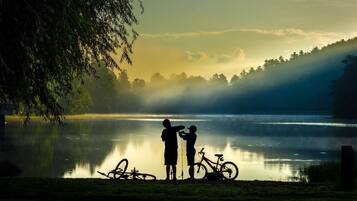 A serene lakeside scene with two people fishing and bicycles nearby.