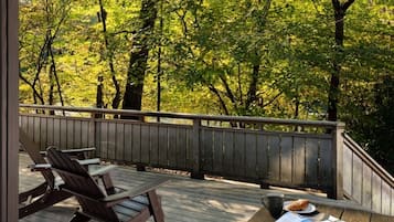 Relax on the deck with a view of the surrounding forest, surrounded by two Adirondack chairs and a table.