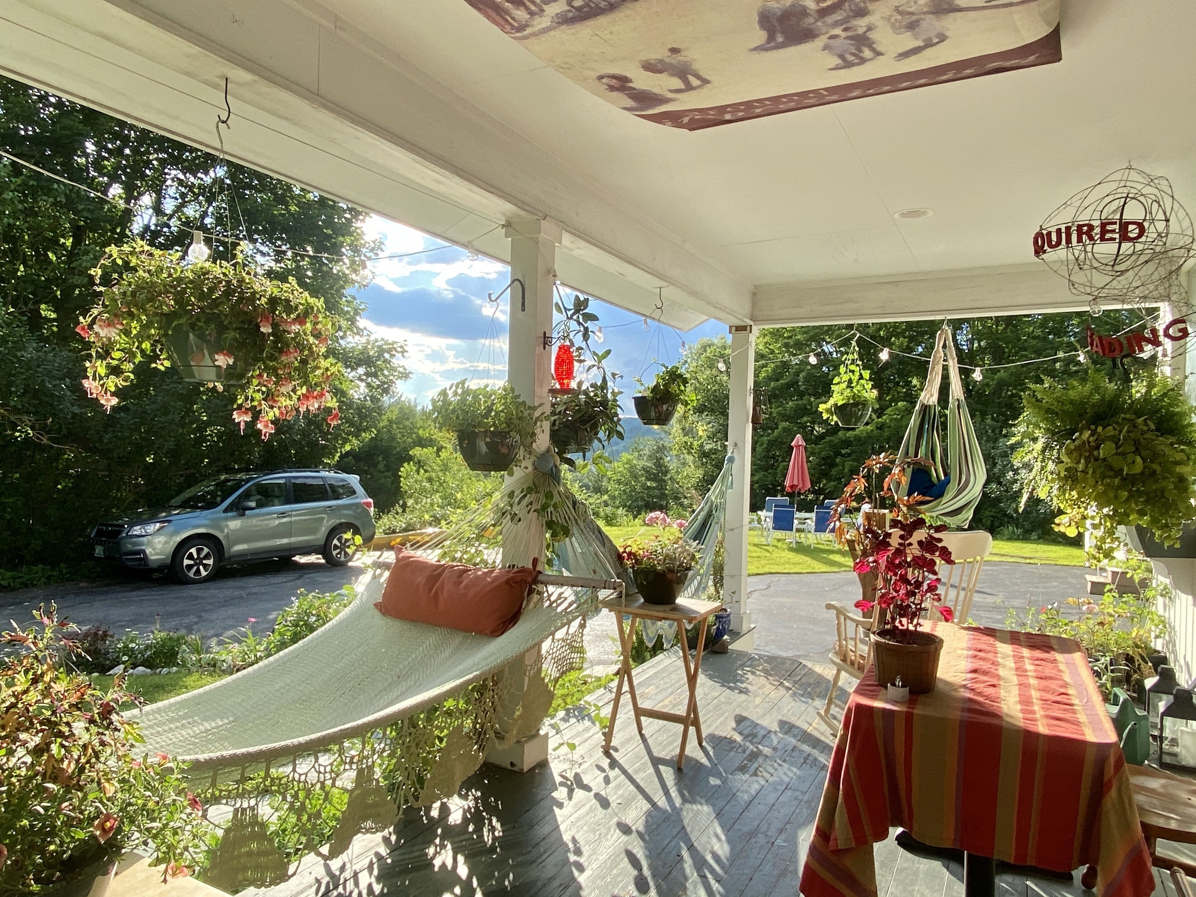 A covered porch with a hammock, outdoor seating, and potted plants.