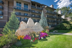 A multi-story building with balconies, a landscaped garden with colorful flowers, and a sign reading 'Vantage Point 508 East Lionshead Circle.'