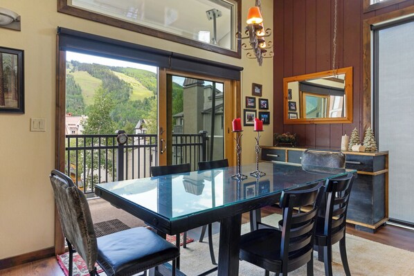 A dining area with a glass table, black chairs, and a view of the outdoors through large sliding doors.