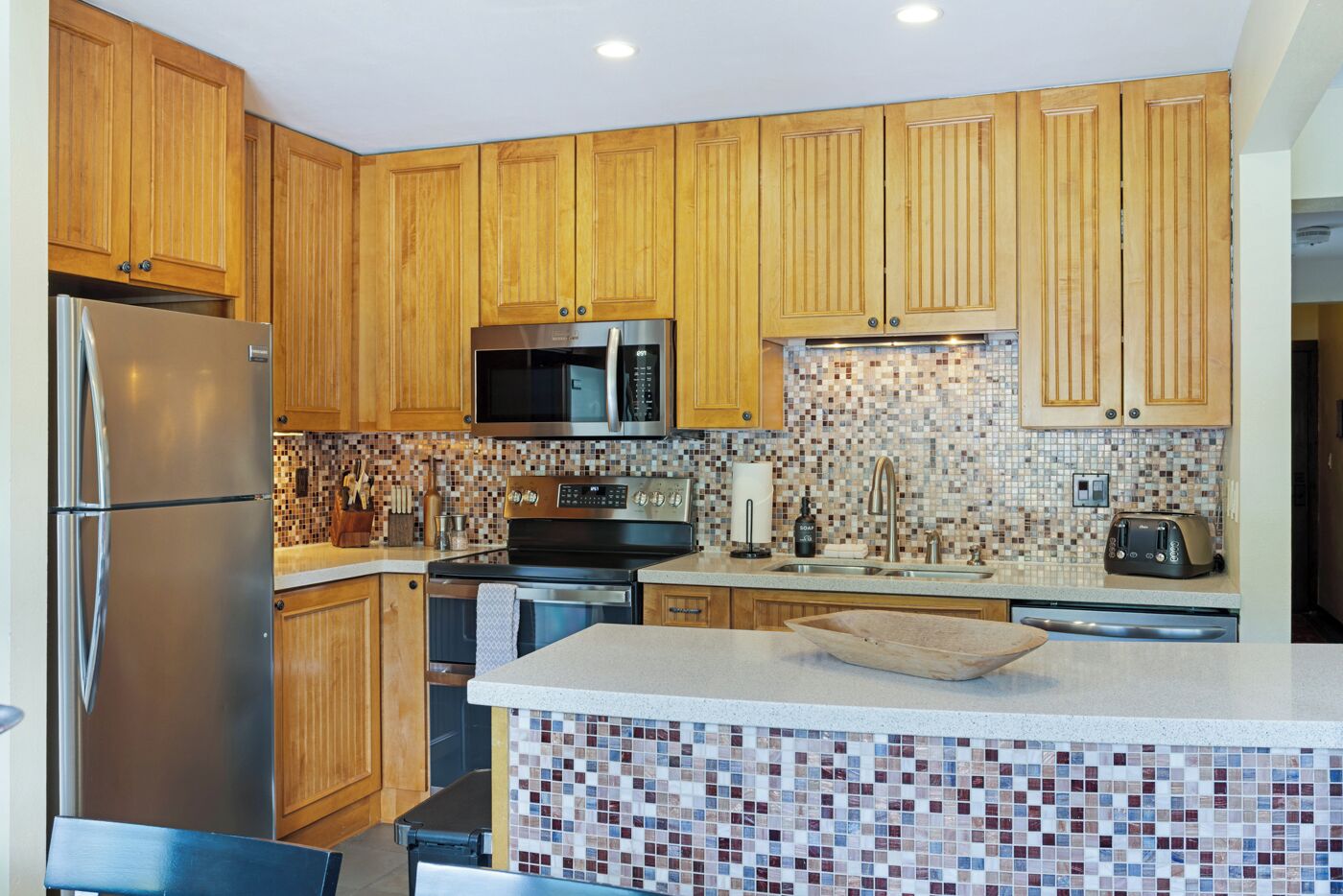 A kitchen with wooden cabinets, stainless steel appliances, a tiled backsplash, and a central island.