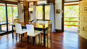A dining area with a wooden table and chairs, a ceiling fan, and large windows with curtains.