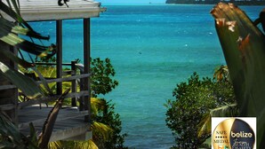 A view from a wooden deck overlooking turquoise waters, with a distant island and lush greenery.