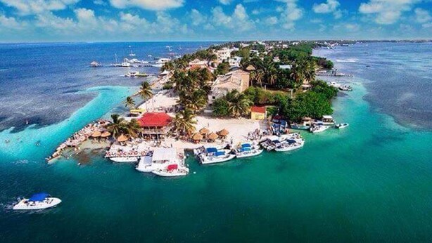 An aerial view of a tropical island with a beach, boats, and a small building with a red roof.