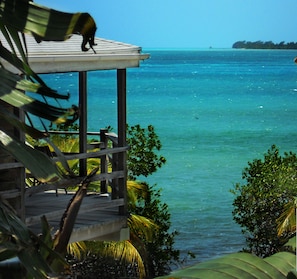 A view from a wooden deck overlooking turquoise waters, with a distant island and lush greenery. - OCEANFRONT ECO-CHIC HOME WITH INFINITY POOL, DOCK, AIR CONDITIONER & TV (Caye Caulker)