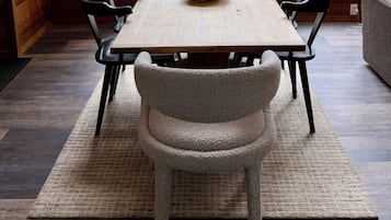 A dining area with a wooden table, six chairs, a bowl, and a view of the outdoors through large windows.