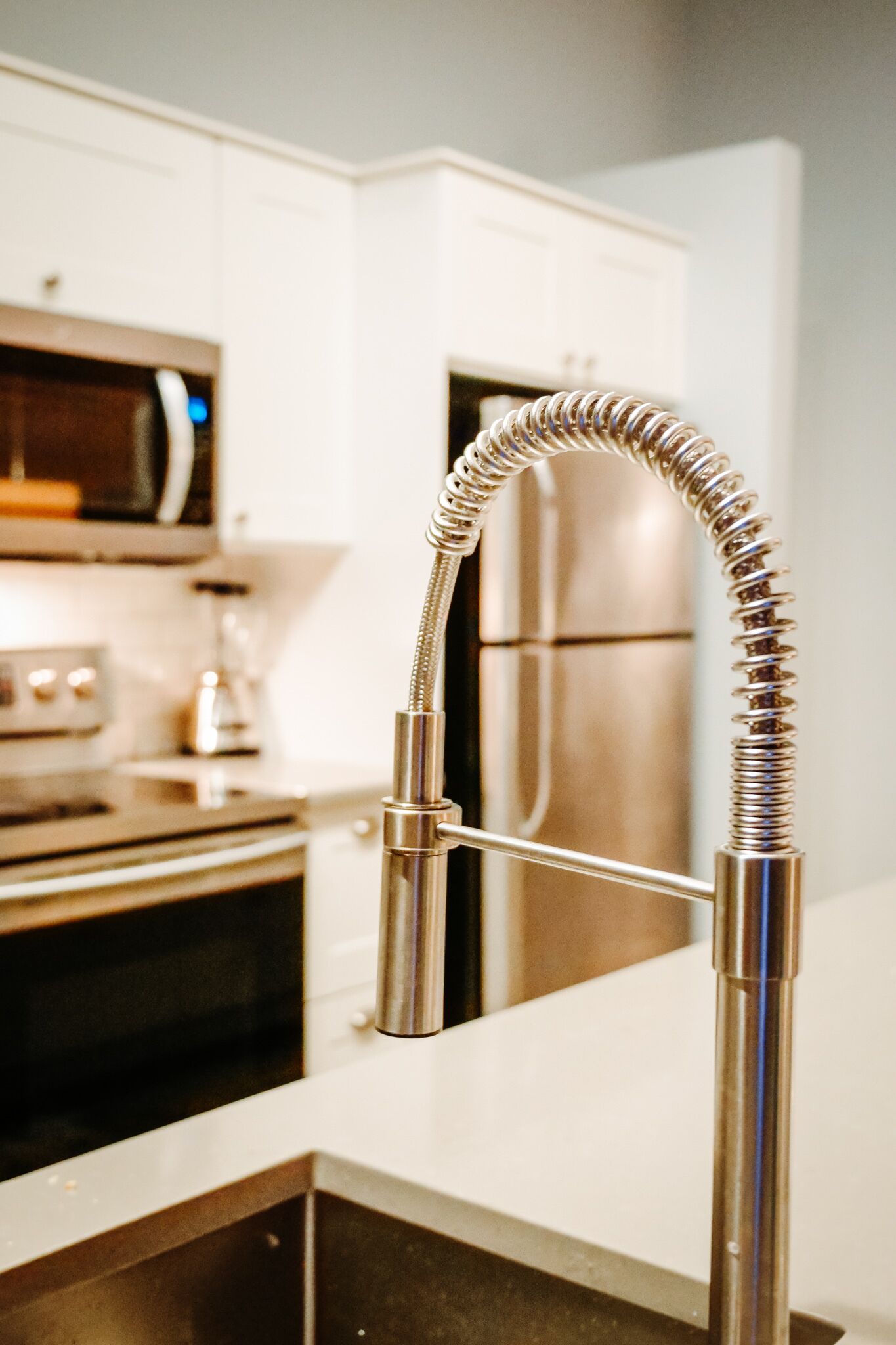 A kitchen with a stainless steel refrigerator, a microwave, and a modern faucet with a flexible hose.