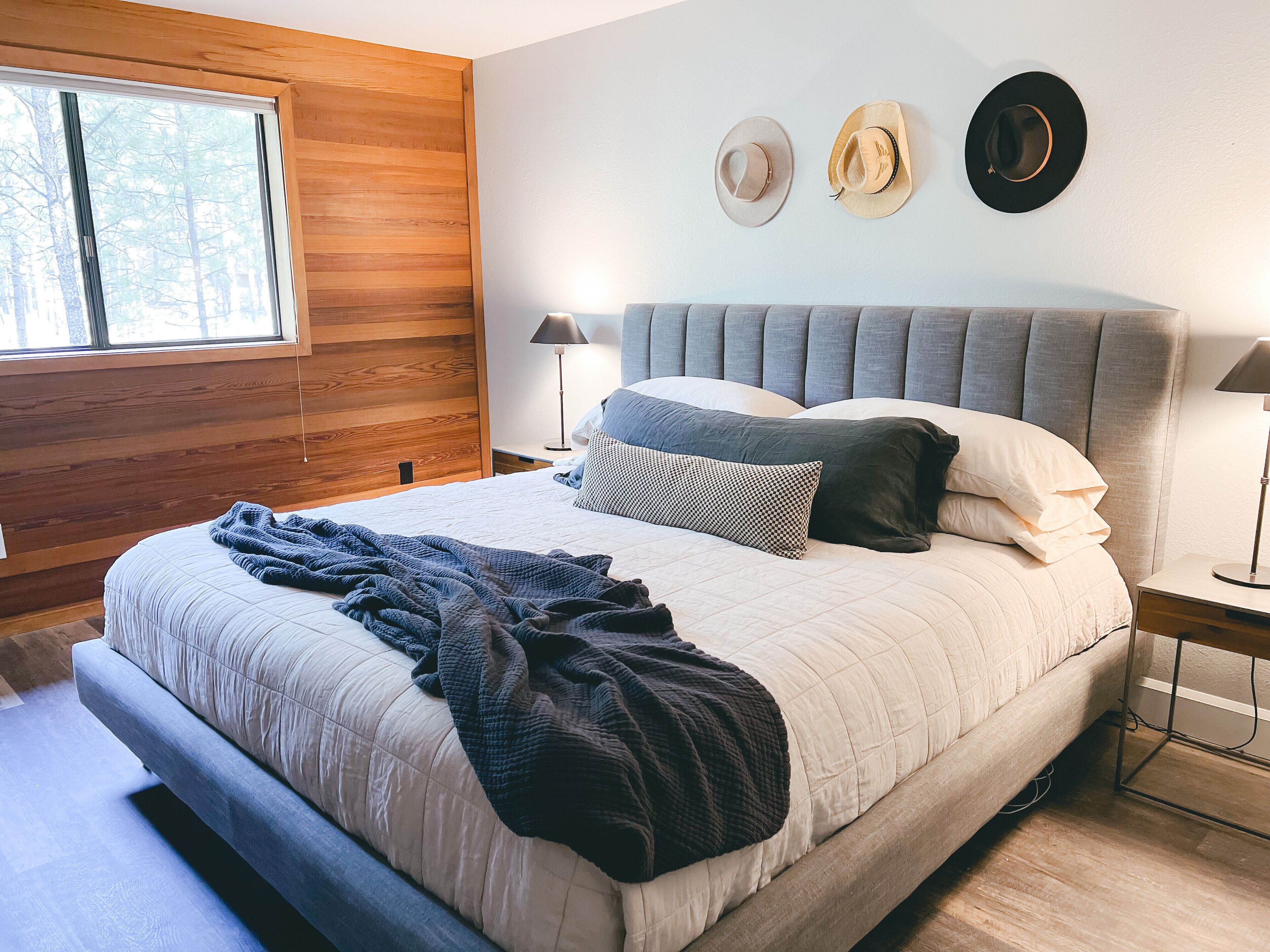 A bedroom with a large bed, a wooden wall, and two hats on the wall.