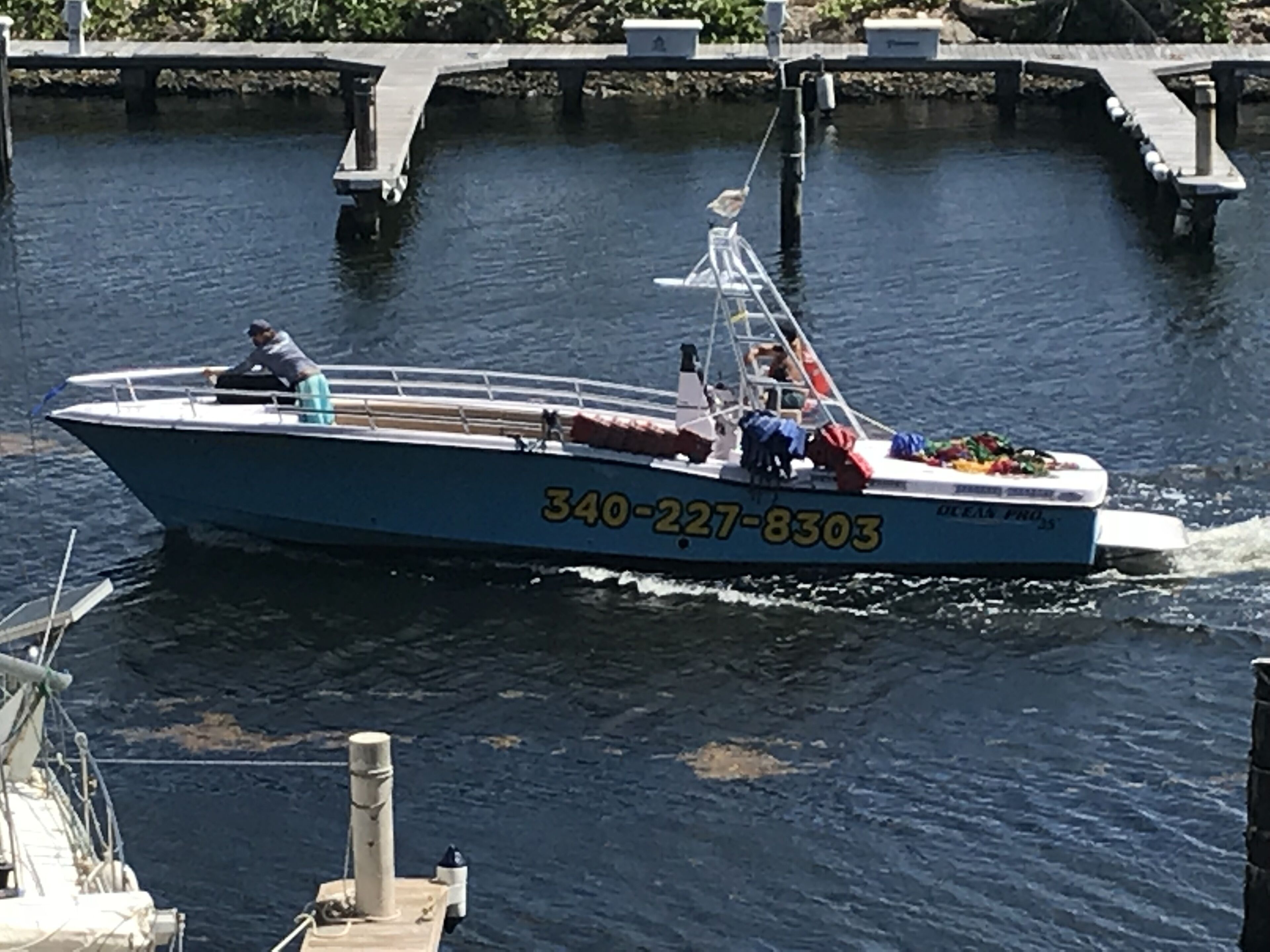 A speedboat with the number 340-227-8303 on its side, docked at a pier with a bridge in the background.