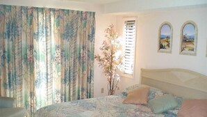Een slaapkamer met een bed, gordijnen, een raam en twee foto's aan de muur.