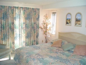 A bedroom with a bed, curtains, a window, and two wall-mounted pictures.