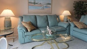 Een woonkamer met een lichtblauwe bank, twee glazen salontafels en twee lampen.