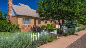 A two-story house with a brick chimney, a white picket fence, and a well-maintained lawn. - Classic Utah Home (Kanab)