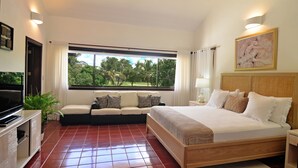 Una habitación de hotel con cama, sofá, televisión, ventana con vista a árboles y un cuadro en la pared.