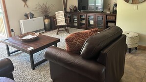 Uma sala de estar com um sofá de couro marrom, uma mesa de centro de madeira, uma televisão e um armário com portas de vidro.
