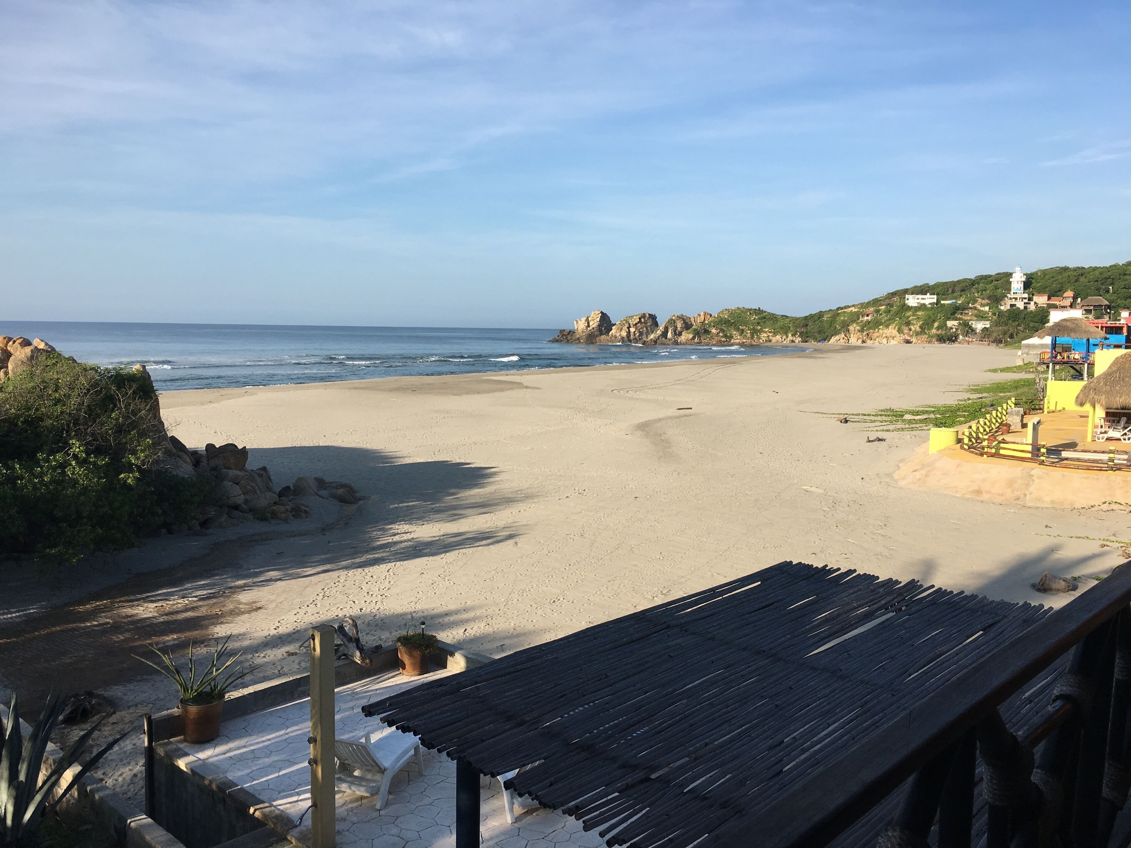 A beach with a wooden structure, a chair, and a potted plant.