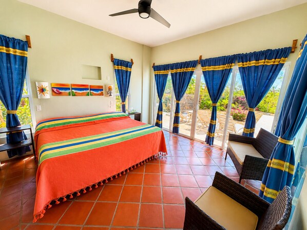 A hotel room with a bed, a desk, and a chair. There is a window with curtains and a view of the outside. - Beachfront Villa C/W Private Pool 3BR/3.5 BA on Secluded Beach (Huatulco)