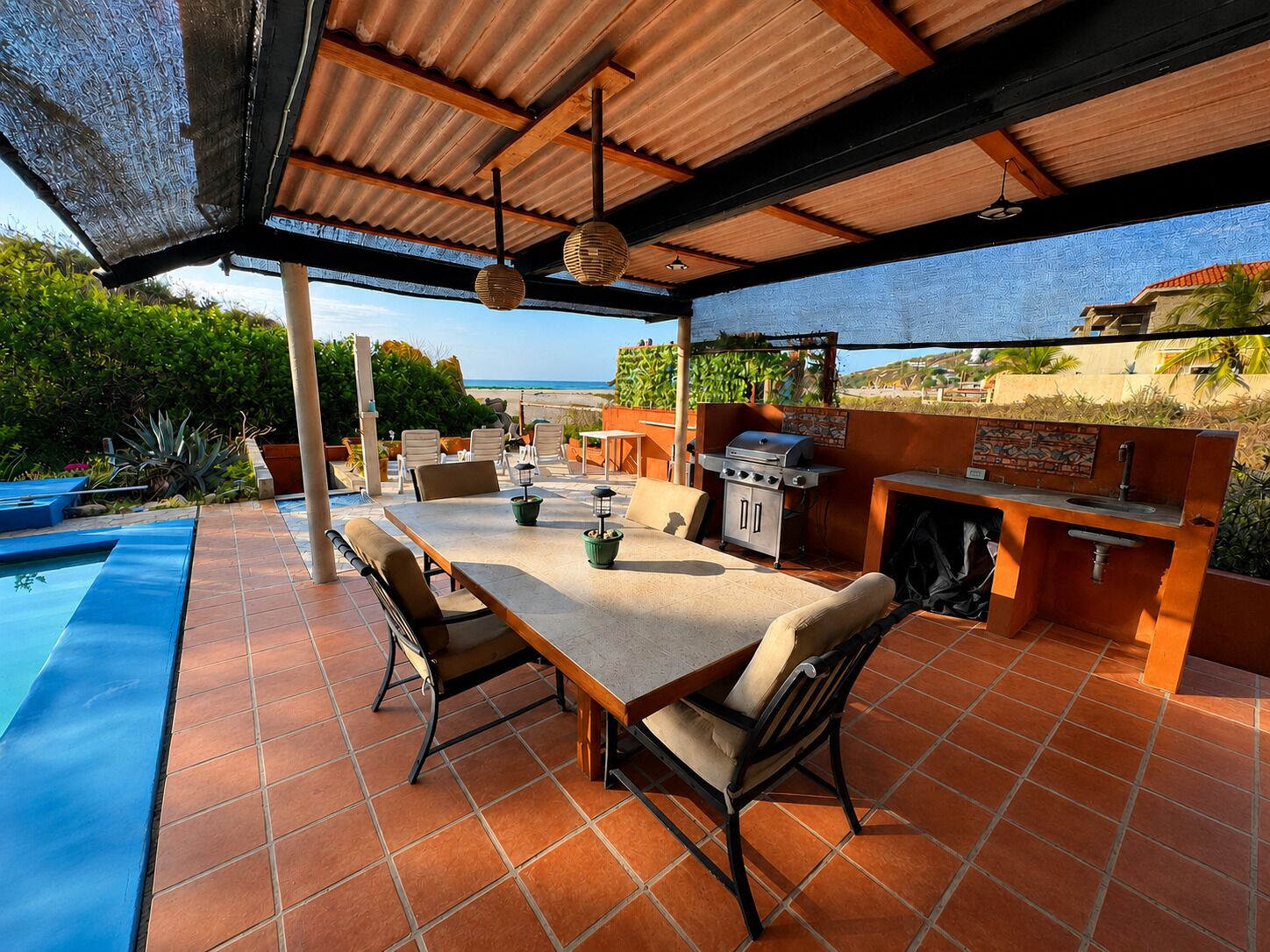 An outdoor patio with a dining table, chairs, a grill, and a view of the ocean.