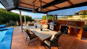 An outdoor patio with a dining table, chairs, a grill, and a view of the ocean.