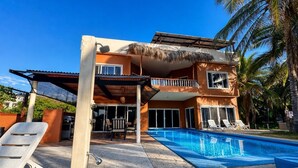A two-story building with a swimming pool, outdoor seating, and a thatched roof structure. - Beachfront Villa C/W Private Pool 3BR/3.5 BA on Secluded Beach (Huatulco)