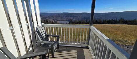 A covered porch with a view of a lake and mountains.