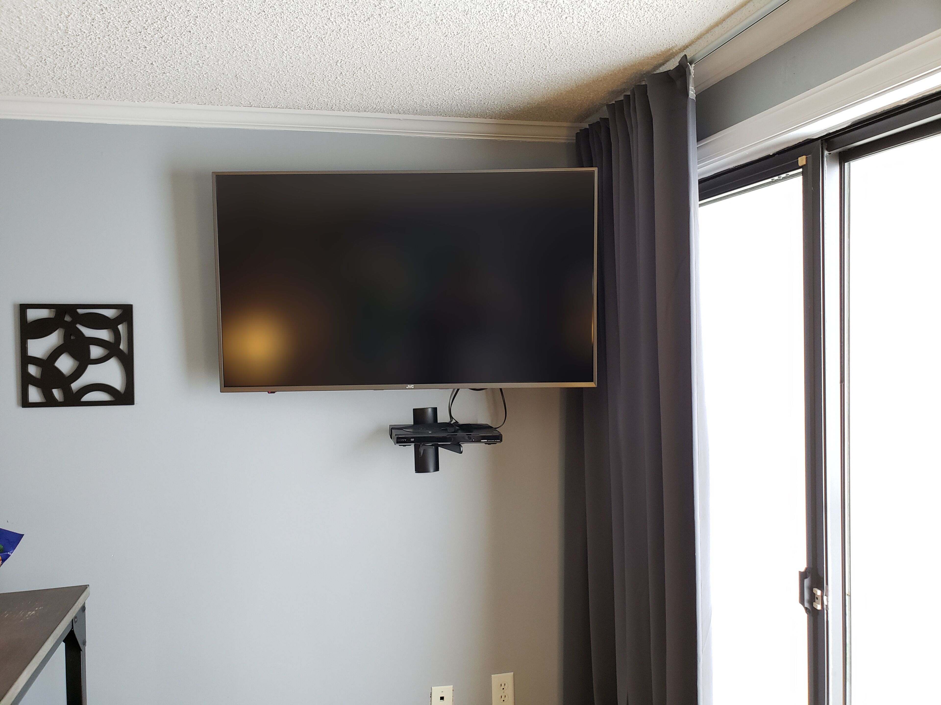 Une chambre dotée d’un téléviseur à écran plat fixé au mur, d’une prise de courant et d’une porte-fenêtre coulissante.