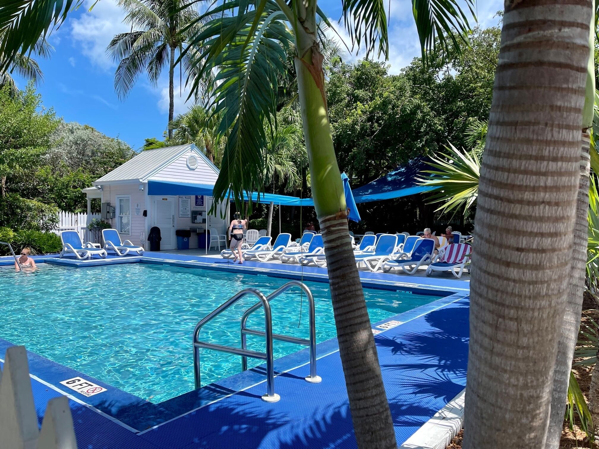 A pool area with blue lounge chairs, a lifeguard tower, and a small building with a blue roof.