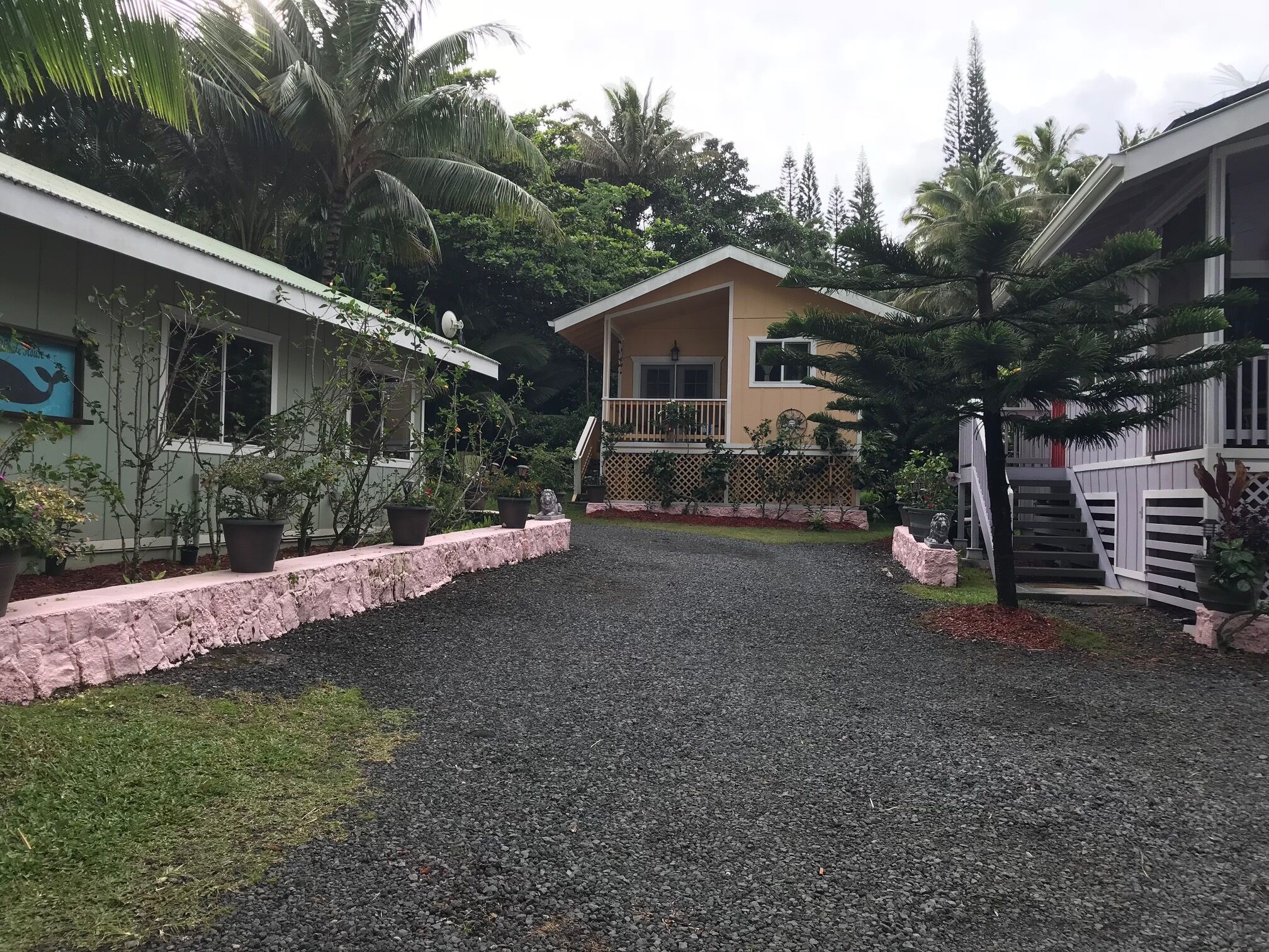 Zona residencial con camino de grava, una casa con balcón y un jardín con plantas en macetas.