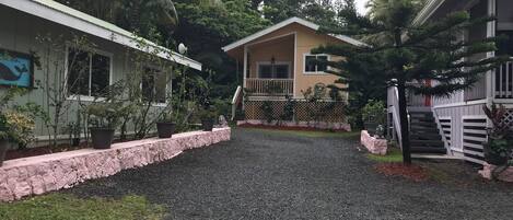 Zona residencial con camino de grava, una casa con balcón y un jardín con plantas en macetas.