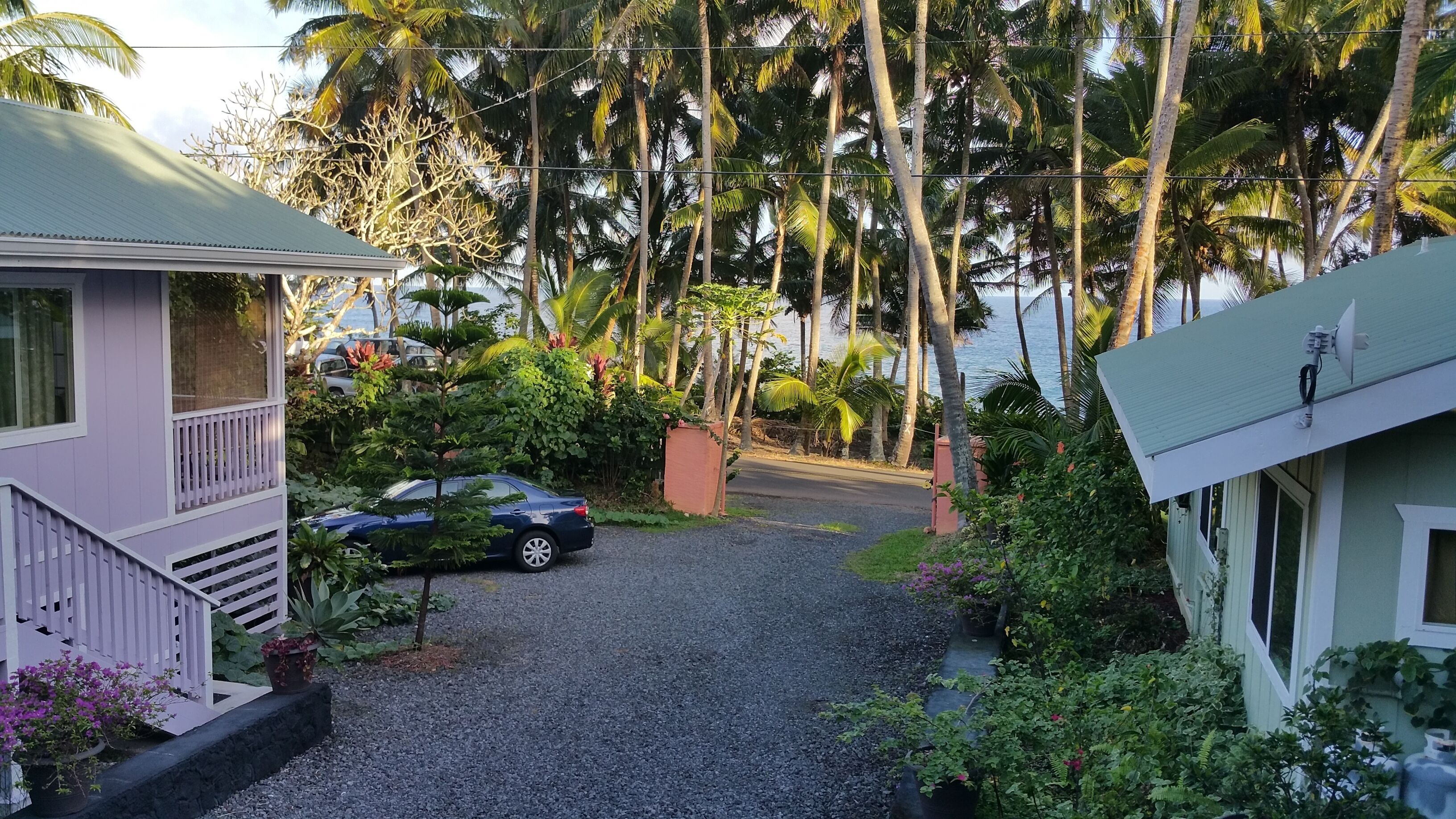 A residential area with a gravel driveway leading to a car parked near a house with a balcony.