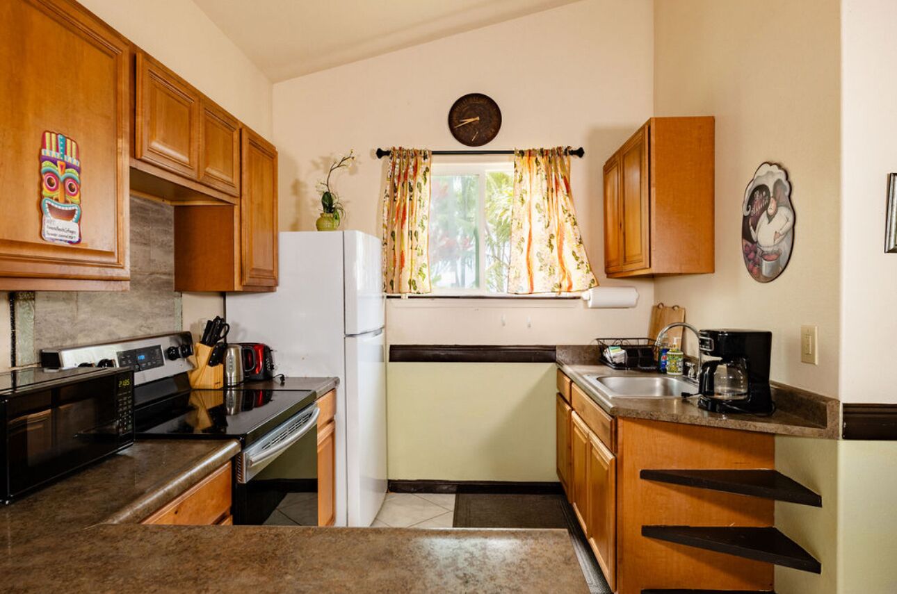 Une cuisine de taille réduite, dotée de meubles en bois, d’un four à micro-ondes, d’une cuisinière, d’un réfrigérateur et d’une fenêtre avec des rideaux.