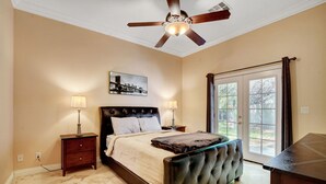 A bedroom with a bed, two bedside tables, a ceiling fan, a large window, and a door.