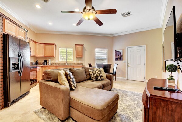 A spacious living area with a sectional sofa, a ceiling fan, and a kitchen in the background.