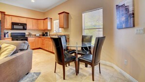 A modern kitchen with wooden cabinets, a microwave, and a dining area with a glass table and leather chairs.